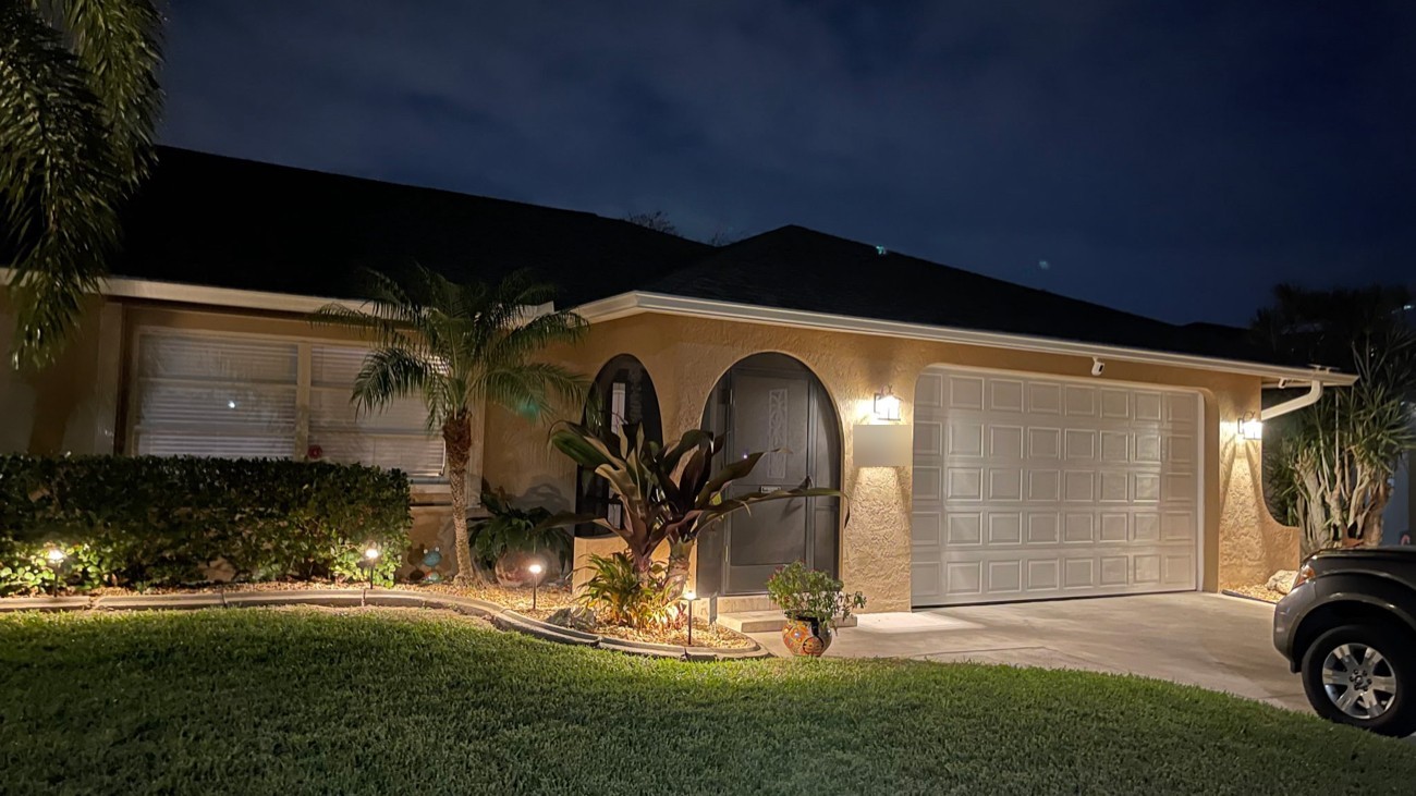 Outdoor wall sconces and low-voltage bed lighting across the arched entry and garage of a Cape Coral home at night