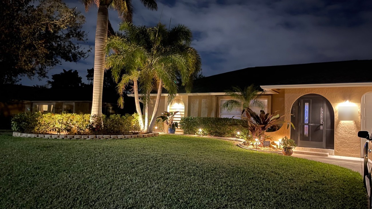 Landscape lighting uplighting tall palms and garden beds in the front yard of a Southwest Florida home at night