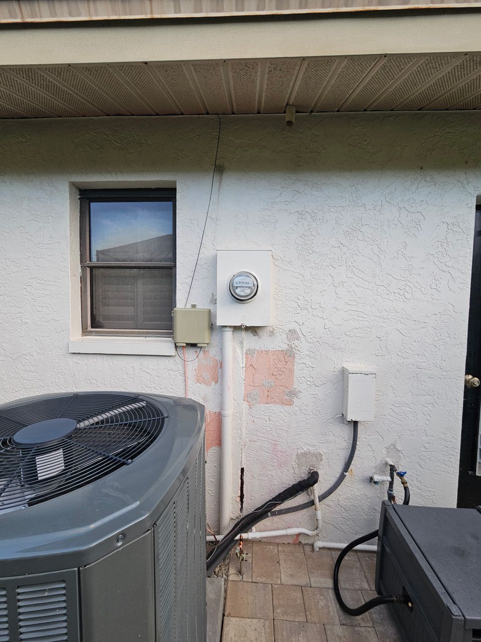 Old white electric meter box on a stucco wall with a single conduit and patched paint, before the upgrade