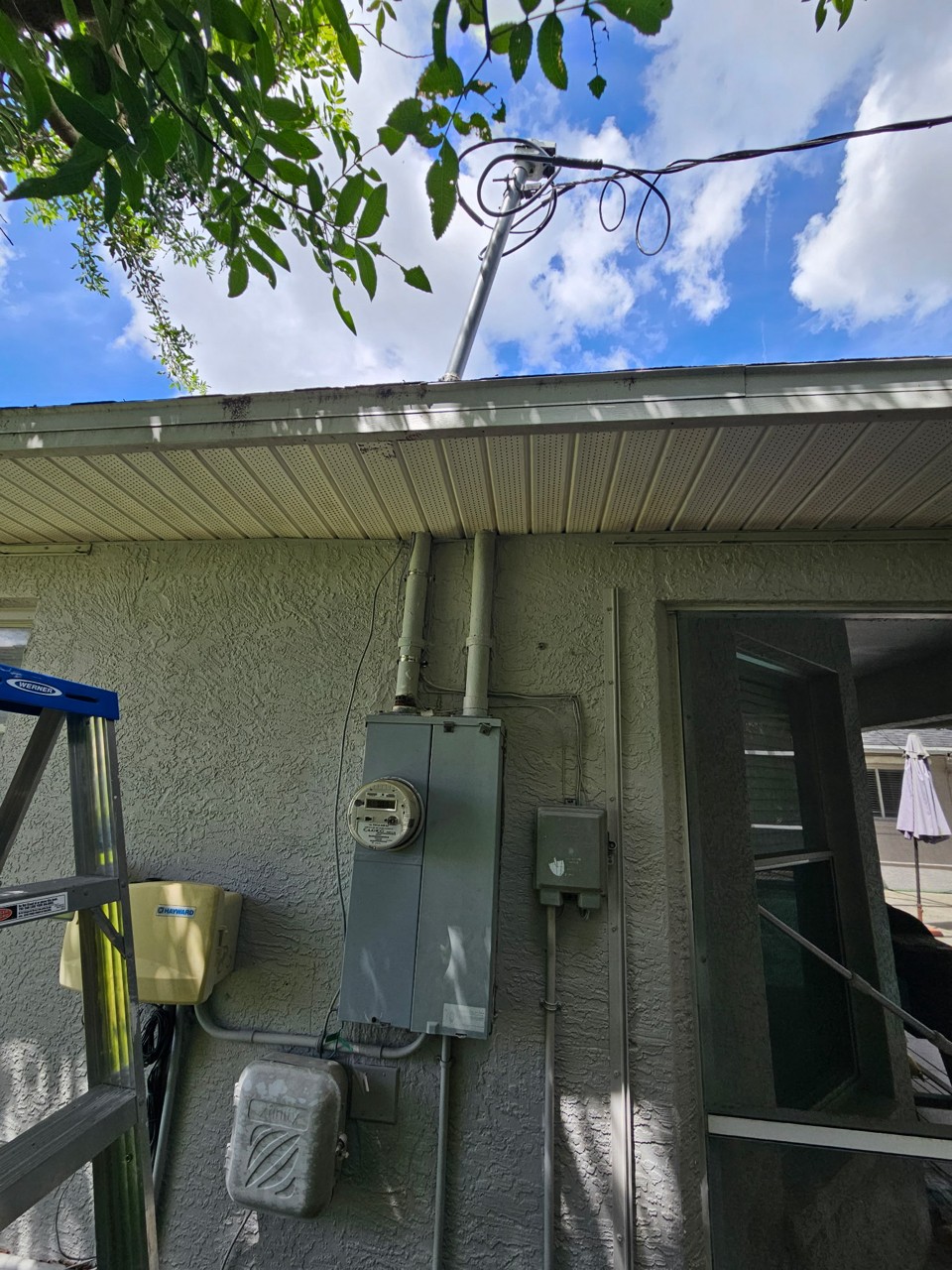 Bent electrical service riser leaning off plumb with a tangled service drop before repair in Cape Coral