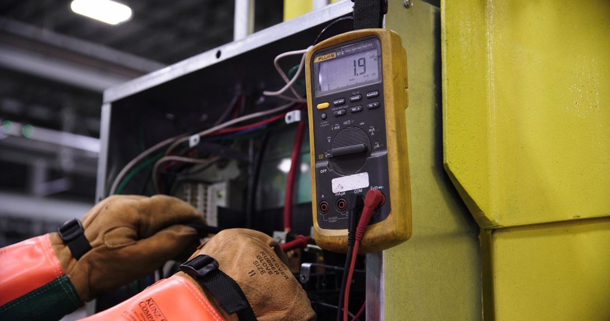 Electrician using a multimeter to diagnose a live electrical panel